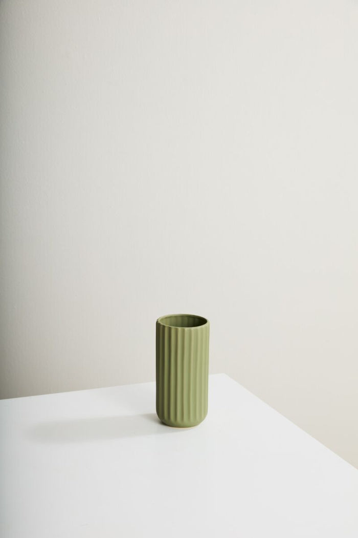 Green ceramic vase on a white surface with a plain background