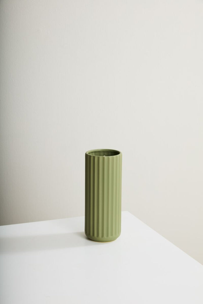 Green ceramic vase on a white surface with a plain background