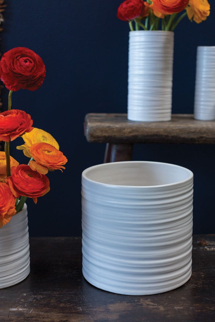 White ribbed ceramic vase with flowers on a dark surface and background