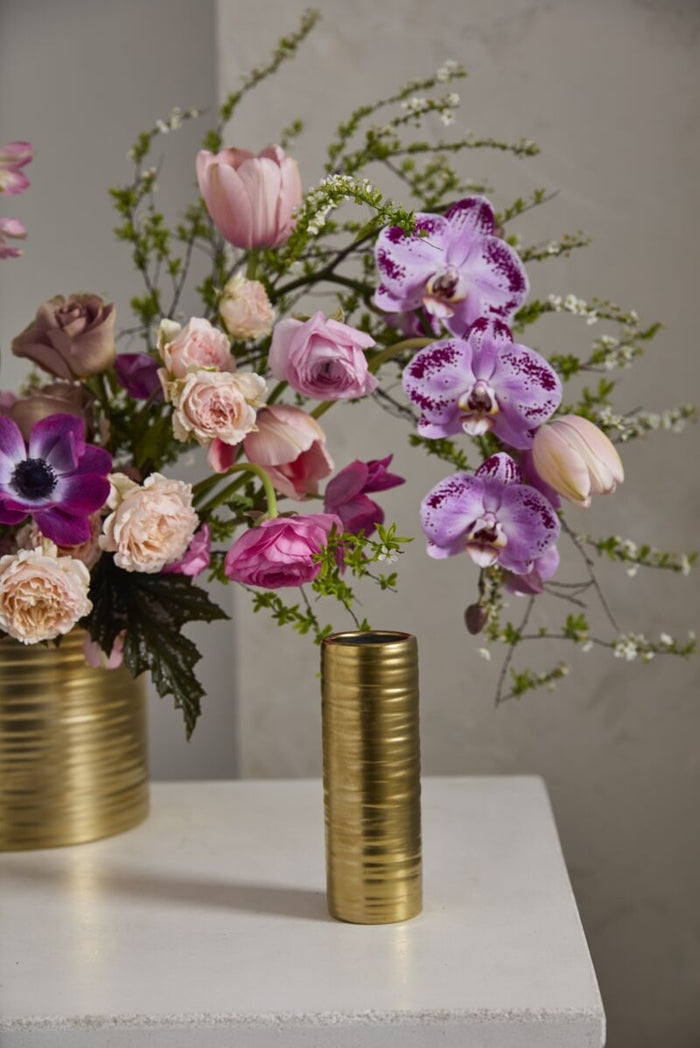 Two gold vases with colorful flowers on a light surface against a neutral background