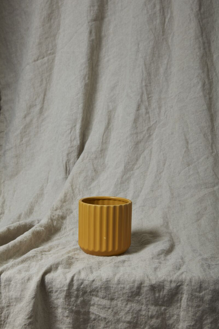 Yellow ceramic pot on a textured beige fabric background