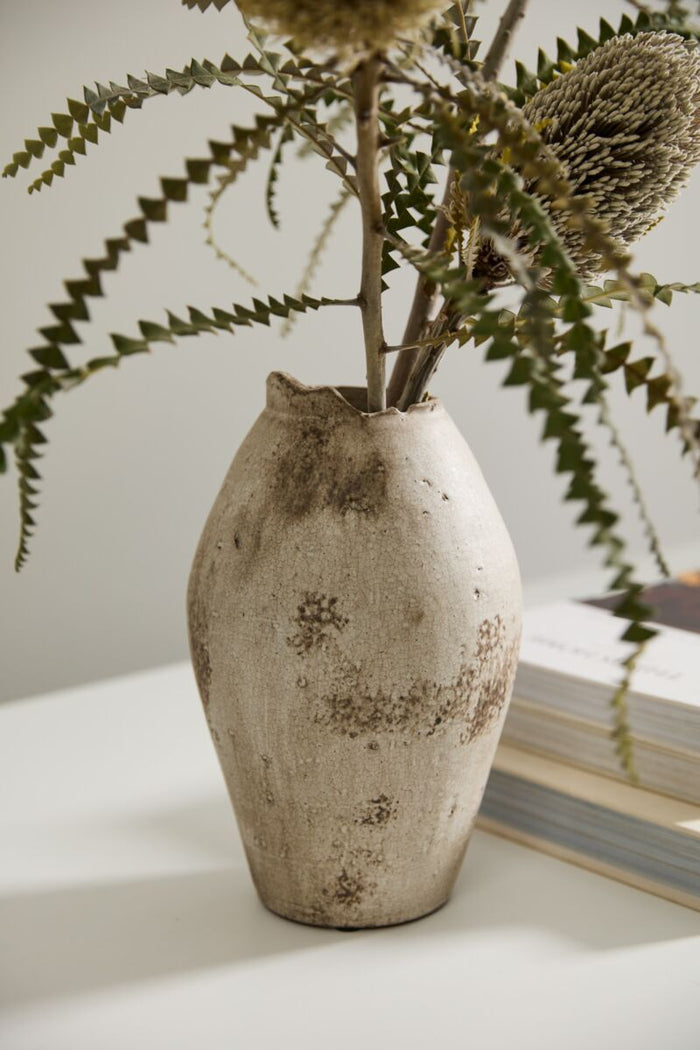 Vintage-style vase with a plant on a light surface