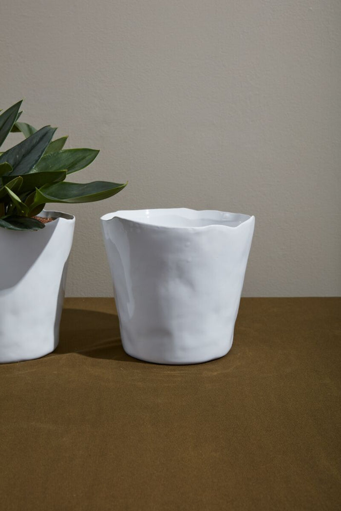 Two white ceramic pots on a wooden surface with a neutral background