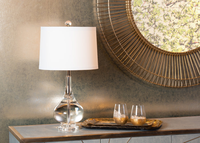 Decorative table setting with a lamp, tray, and glasses against a textured wall.