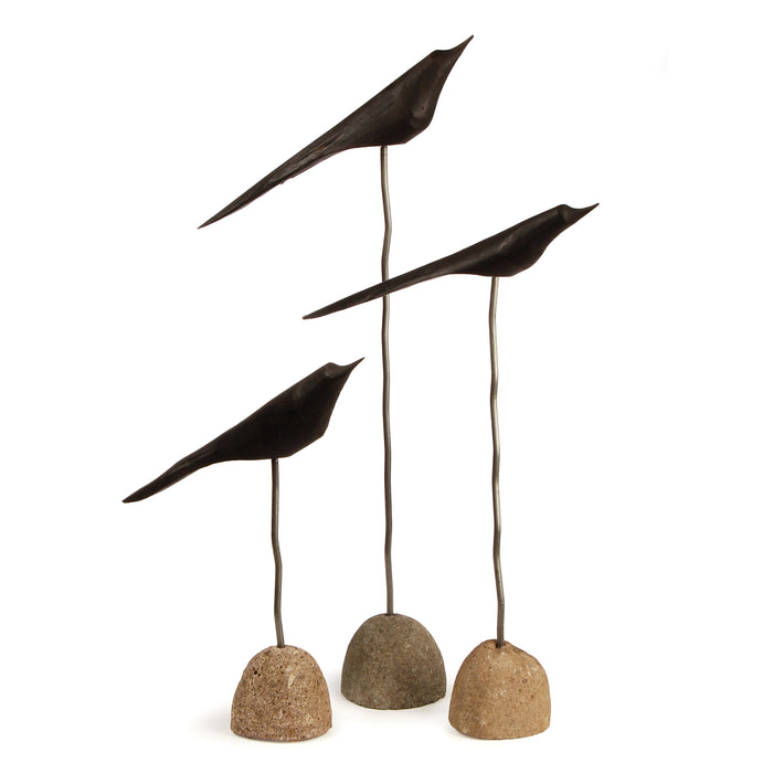 A set of three black bird sculptures on a white background, with two birds perched on cylindrical stands and one in flight above round bases.