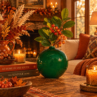 A round, emerald green porcelain bud vase with a glossy finish in a Coco Plum home on a rattan shelf.