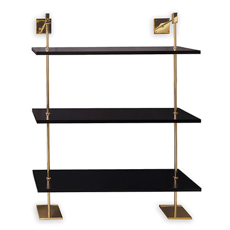 A modern multi-tier shelf with polished gold metal poles and black MDF wood shelves, secured to the wall and designed to rest on the floor.