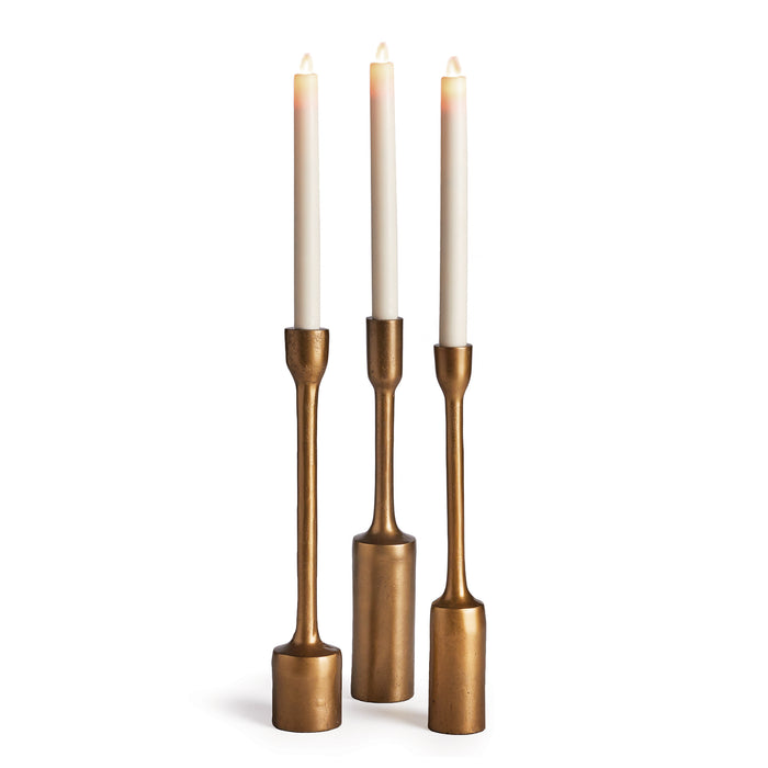A set of three antique brass taper candle holders arranged side by side against a white background.