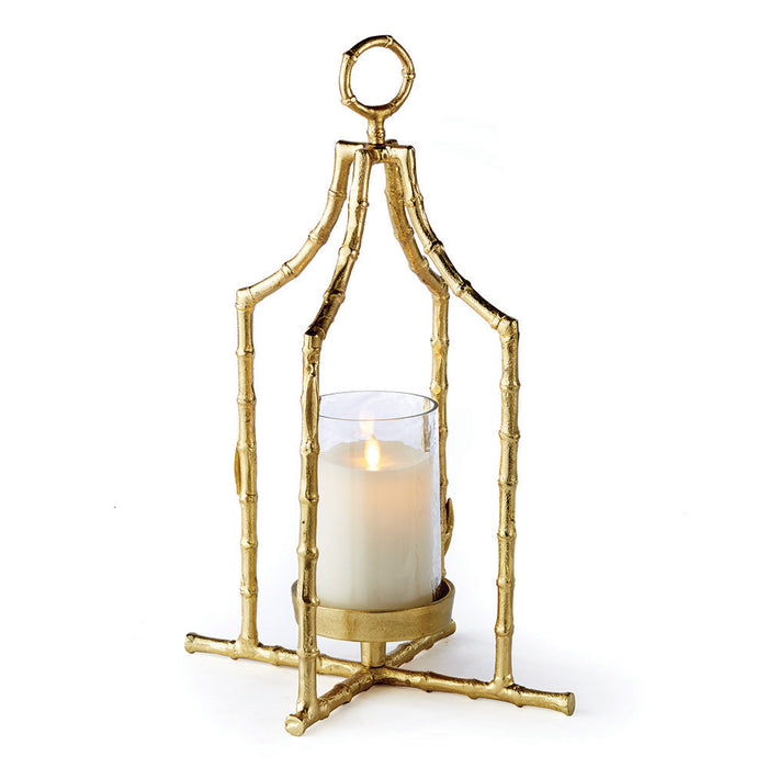 A gold bamboo-like metal lantern with a seeded glass insert, designed to hold a candle. It features a loop for hanging and has a textured frame.