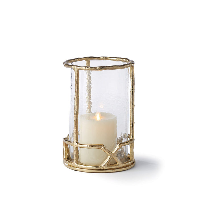 A gold bamboo-like metal candle holder with a clear glass insert and a lit candle inside.