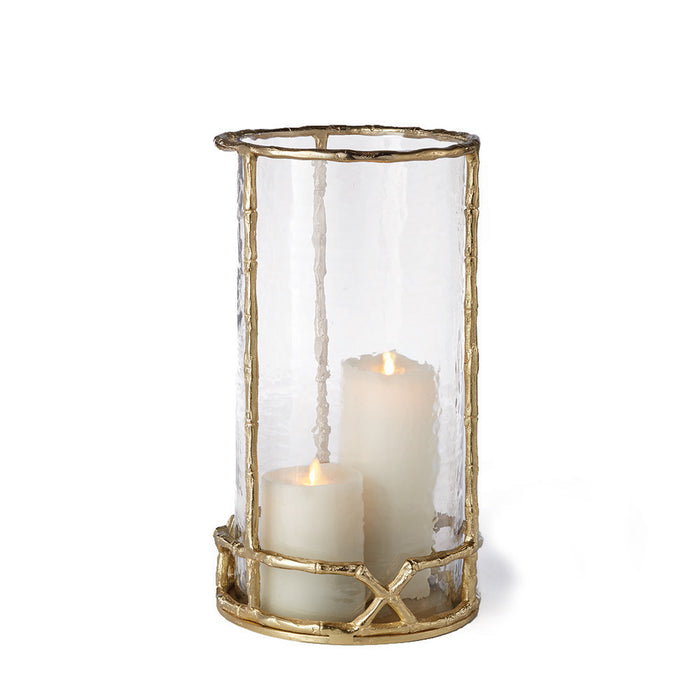 A gold bamboo-like metal candle holder with a clear glass insert containing a candle. The holder has a narrow top and a wide base.