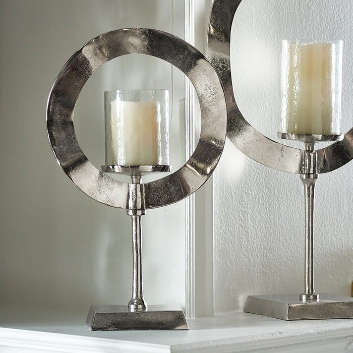 Polished silver circular candle holder with a central glass hurricane and ivory candle, mounted on a square pedestal