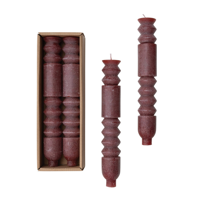 A set of two brown totem taper candles placed inside a cardboard box with a lid.