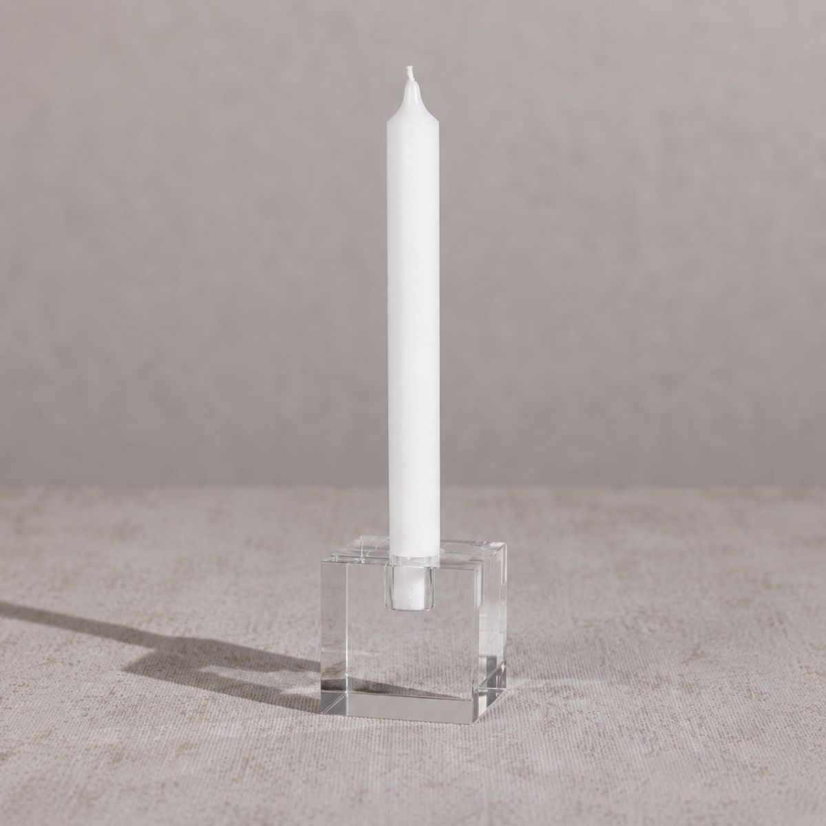 White candle in a clear glass holder on a gray surface with a neutral background