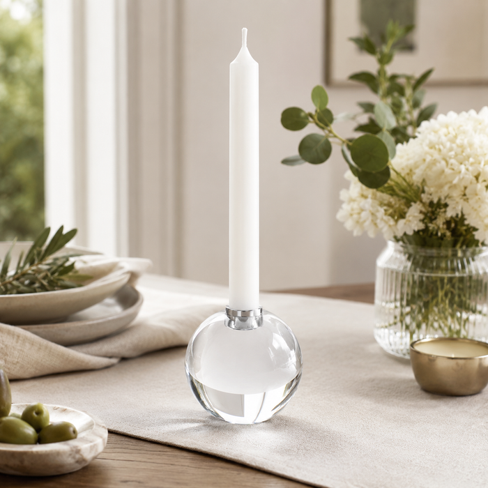 Decorative candle holder with a white candle on a table with a vase of flowers and greenery.