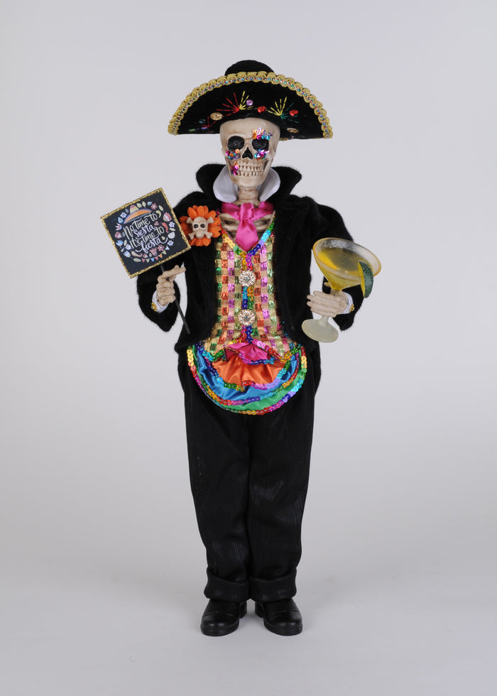 Decorative skeleton figure in a colorful outfit with a sombrero, holding a book and a glass, on a white background.