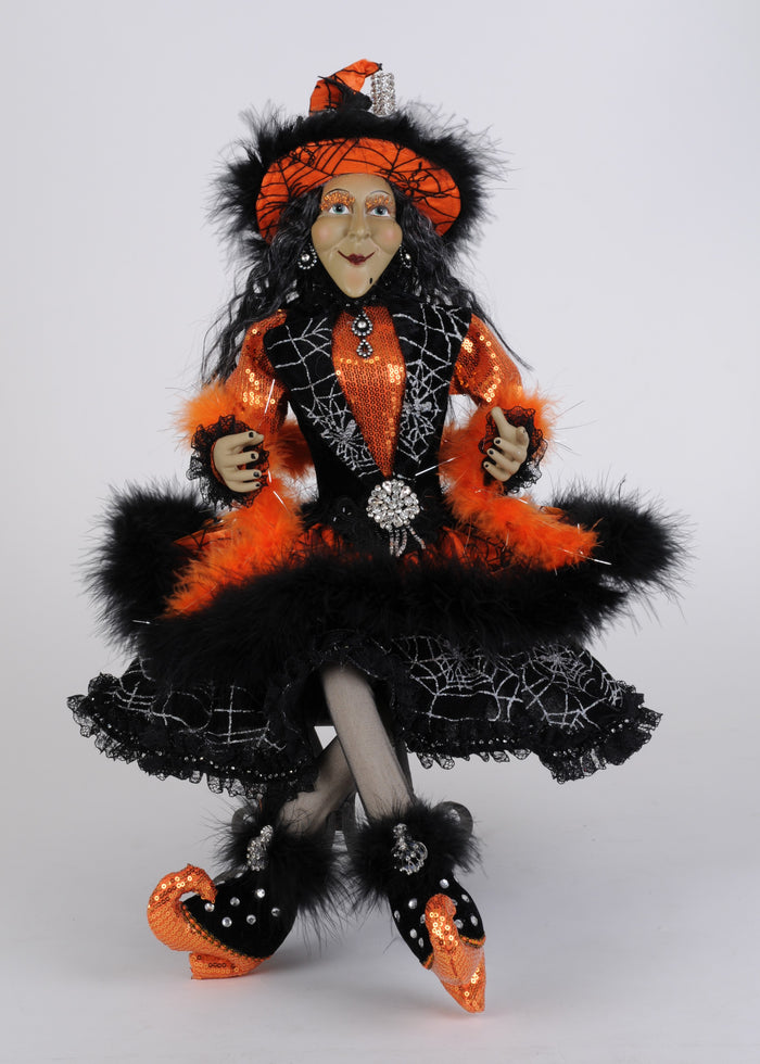 Halloween-themed doll in black, orange, and white outfit with spider web details on a gray background