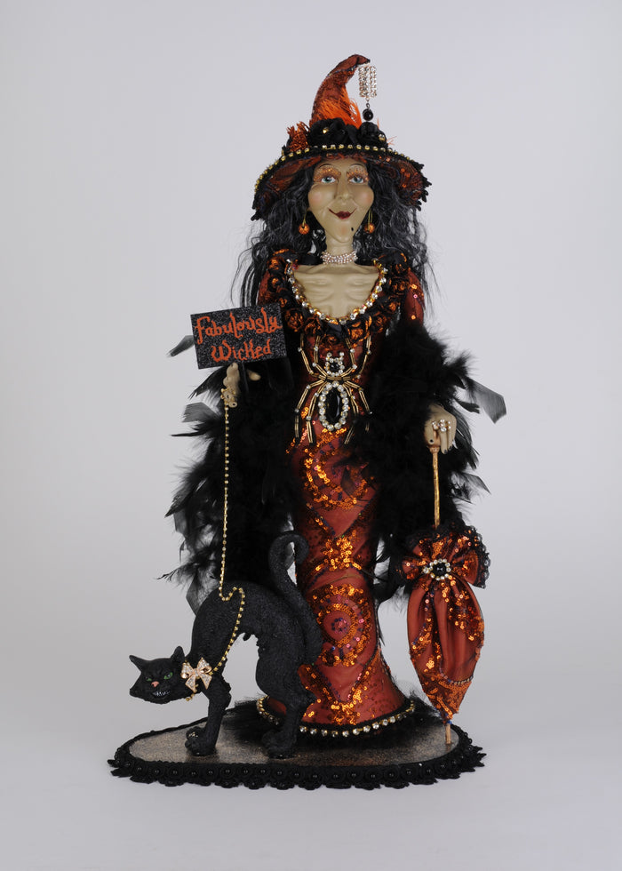 Halloween-themed doll with black cat, orange and black outfit, and feathered headdress on a white background.