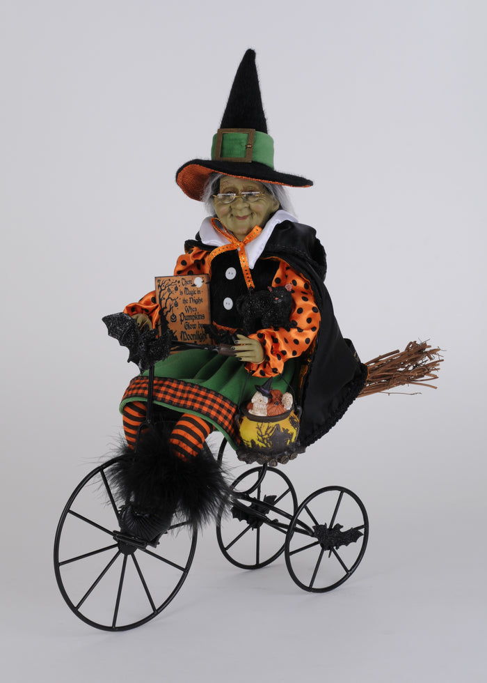 Halloween witch figurine on a tricycle with broom and pumpkin bag.