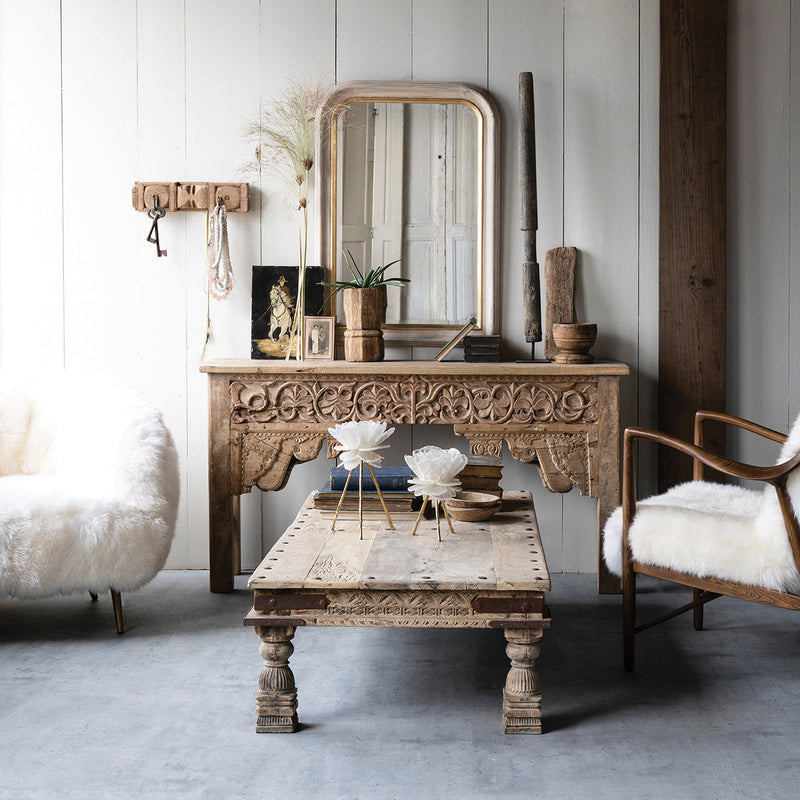 Vintage-style wooden console table with decorative items in a room with a white wall and wooden floor.