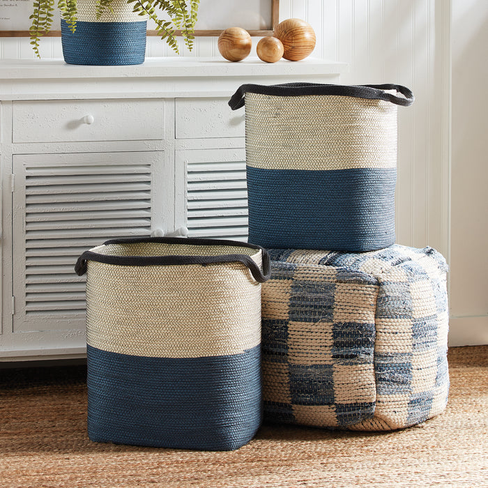 Set of two cylindrical woven baskets with blue and natural beige stripes, black handles, placed on a woven rug by a white