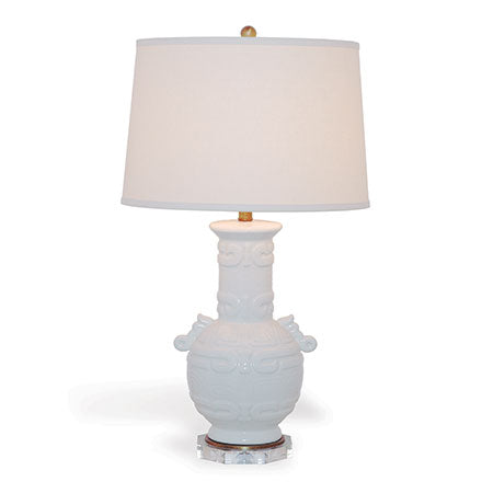 A Tibetan inspired cream crackled porcelain lamp with an octagon shaped lucite base and aged brass hardware. It has a metal ball finial and a white lampshade.