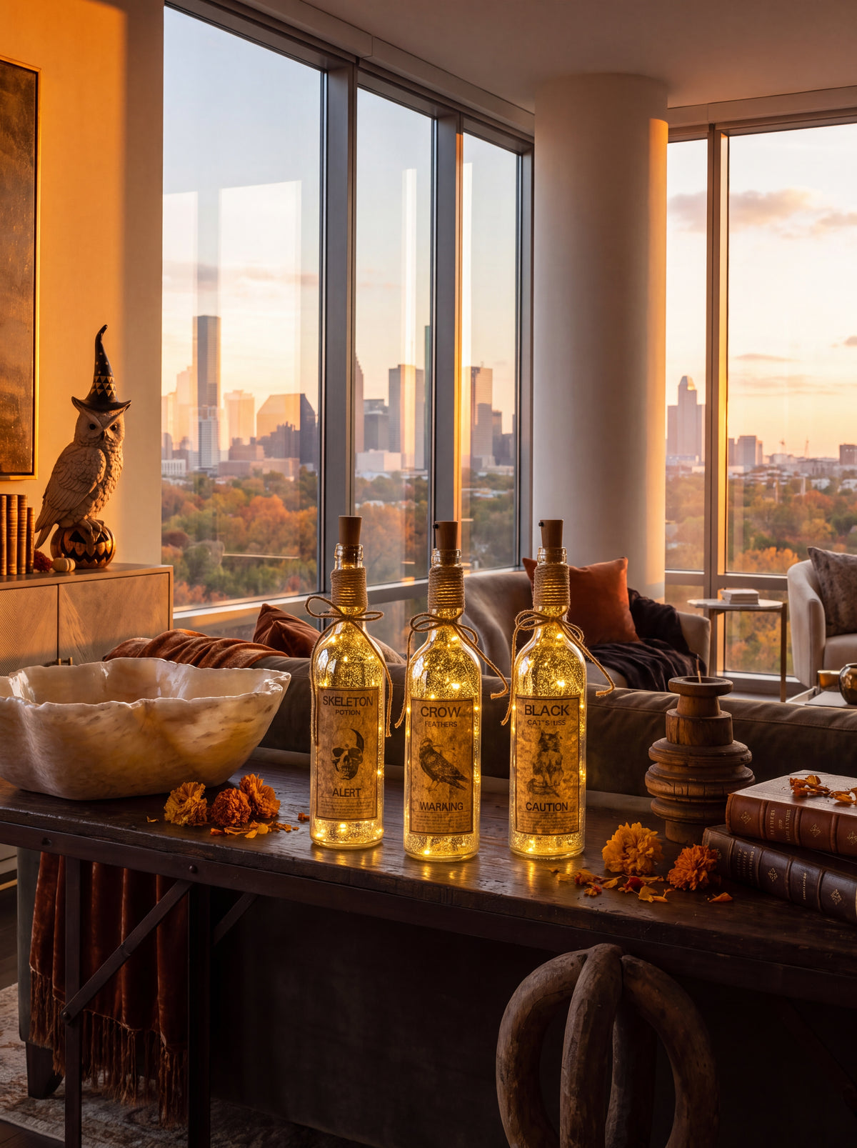 Three decorative glass bottles filled with golden liquid and featuring illustrated labels, displayed on a dark wooden table in a modern living room with a city skyline view through large windows.
