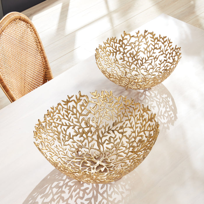 Two gold decorative bowls with intricate coral-like lattice edges on a white table, casting shadows.