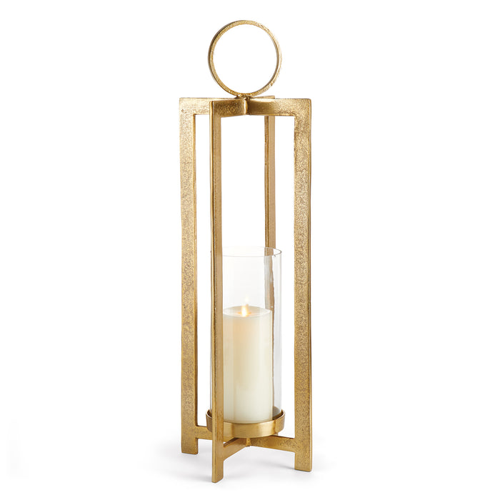 A gold-colored metal lantern with a large round handle and a footed detail, designed to hold a candle.