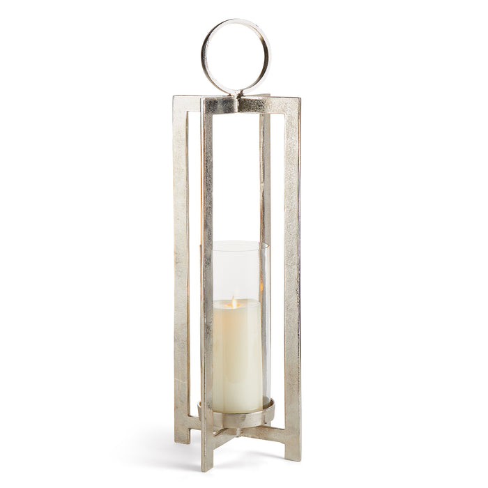 A large metal lantern with a geometric design, featuring a round handle and a footed detail, containing a candle.