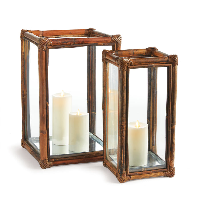 Two solid cane rattan hurricanes with glass panels, designed to hold LED candles, in a warm brown color.
