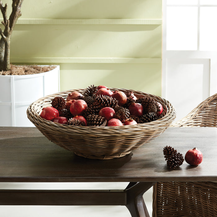Large woven basket filled with red apples and pinecones on a wooden table, bright green wall background.