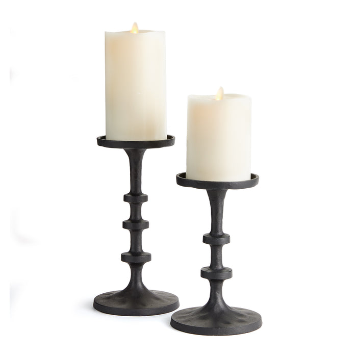 A set of two black aluminum candle stands with a modern design, featuring notches along the body and holding lit candles.