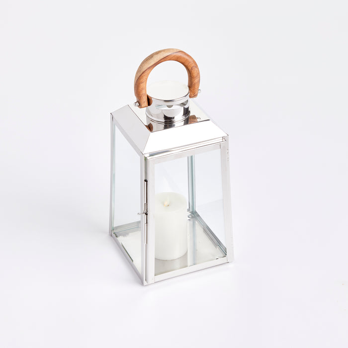 Polished silver metal lantern with glass panes, wooden curved handle, and a white candle inside on a white background.