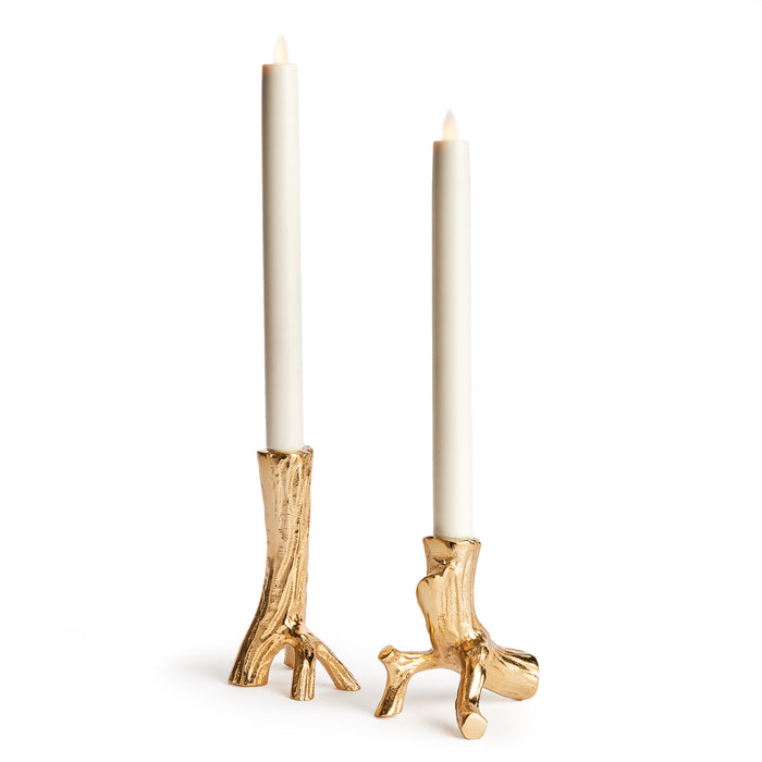 A pair of gold-colored aluminum taper candle holders with a sculpted design, displaying a candle in each holder against a white background.