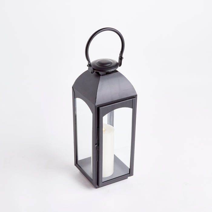 Large black metal outdoor lantern with glass panels and a white pillar candle inside, arched handle on top.