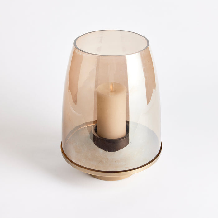 Copper-toned hurricane lantern with glass dome over ivory candle, gold base and ring, plain white background.
