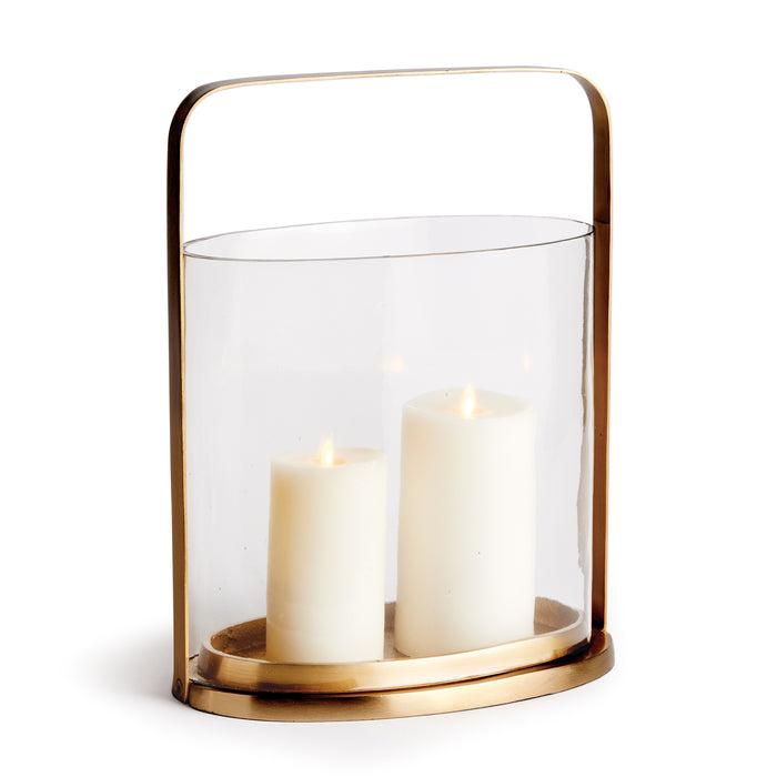 An oval-shaped glass hurricane candle holder with a matte brass frame and two lit candles inside.