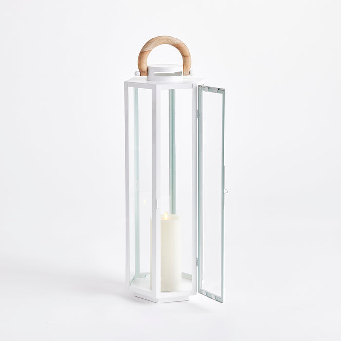 White metal lantern with glass panels, open door, wood arched handle, and a lit pillar candle inside.