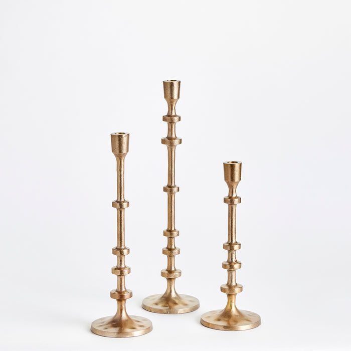 Three brass taper candle holders, varying heights, ornate stacked segments, on white studio background.