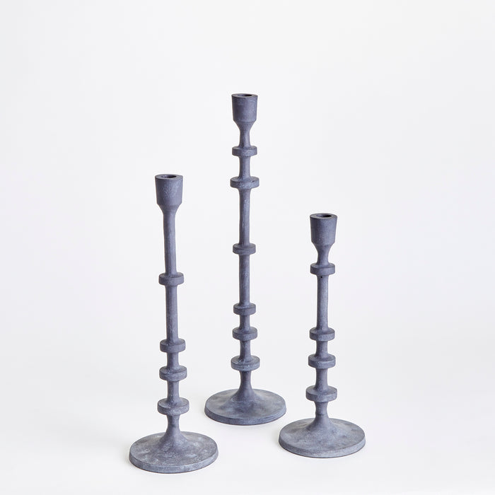 Three tall blue-gray taper-holders with segmented stems and wide bases on a white background, varying heights.