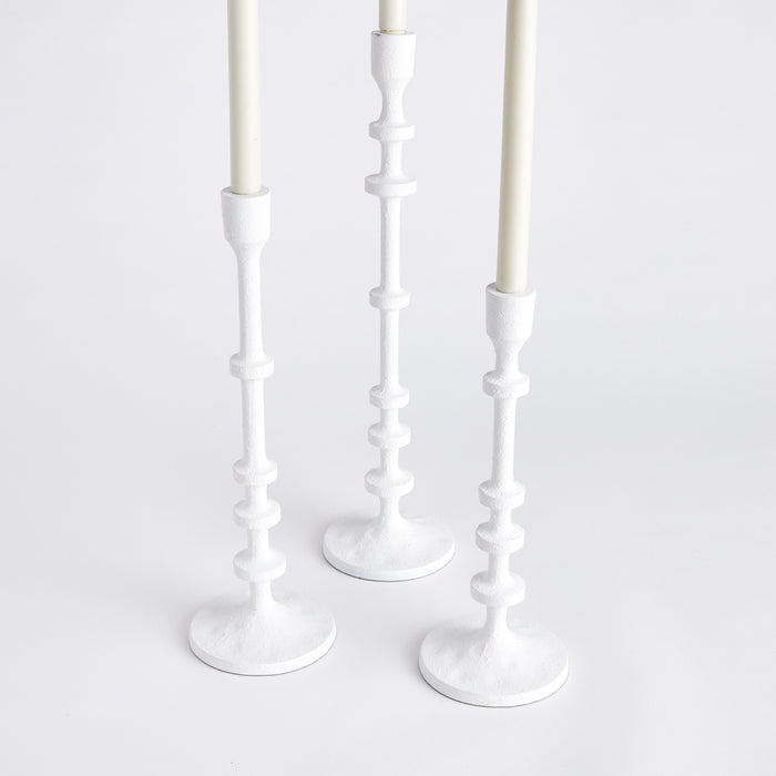 Set of 3 white tapered candlestick holders with ribbed vertical stems on flat round bases, neutral backdrop.
