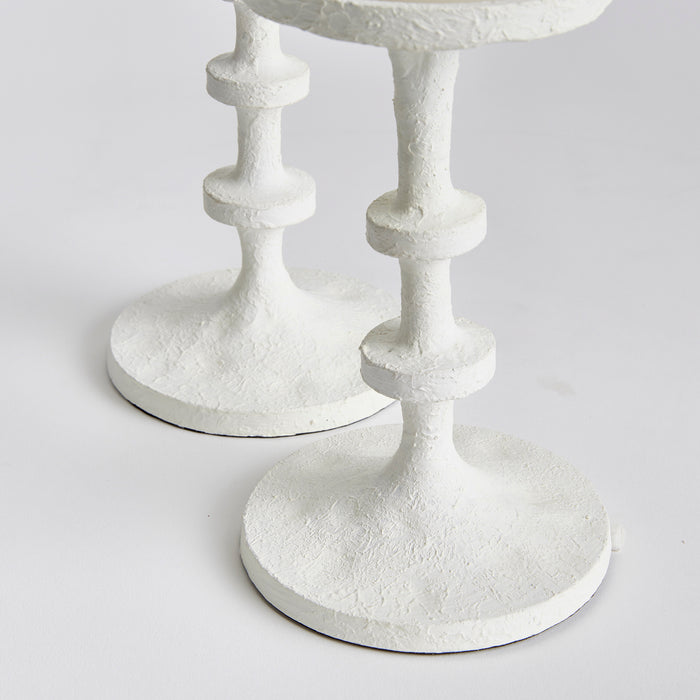 Two white textured candle stands with stacked pedestal stems on round bases, close-up against a light background.