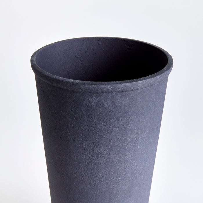 Large dark blue/black terracotta vase with matte finish, wide opening, minimalist cylindrical shape, neutral light backdrop.