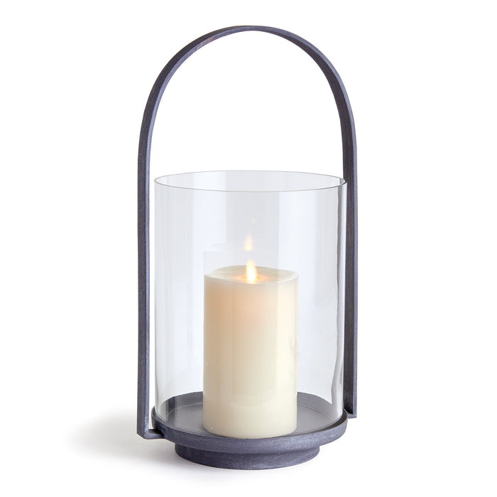 A clear glass outdoor hurricane with a gray metal base and a lit candle inside.