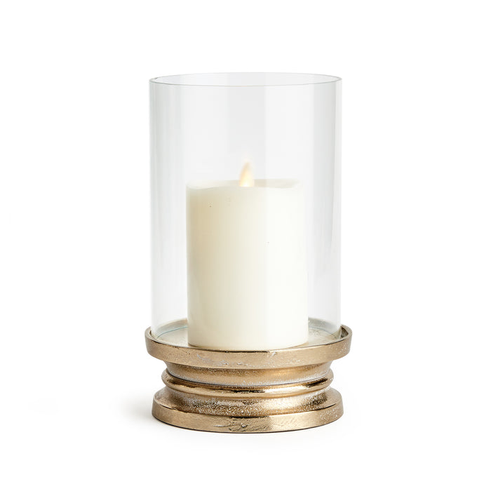 A clear glass hurricane with a brass base, designed to hold a candle. The hurricane has a smooth, clean silhouette with a snow-on-brass finish.