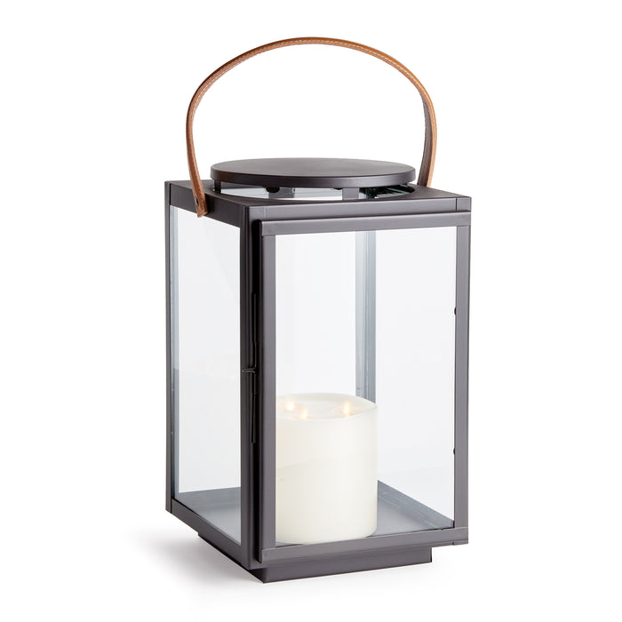 A large lantern with a gray iron frame, clear glass base, and a leather handle with stitching.