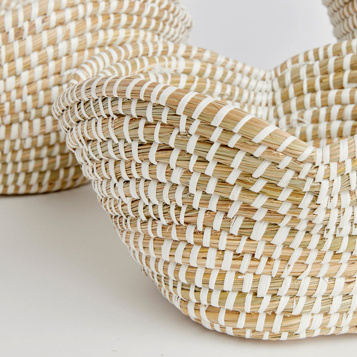 Set of three natural woven baskets with light tan and white palm/raffia strips, close-up showing curved rims and interlaced