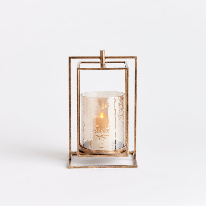 Bronze metal hurricane lantern with hammered glass cylinder, square geometric frame and small handle on top, set against