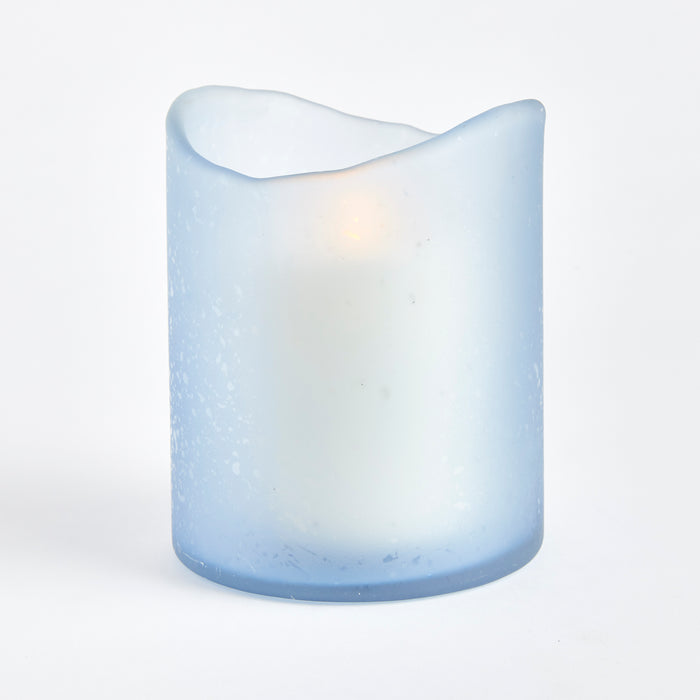 Hurricane Medium blue candle with frosted finish, irregular melted top, glowing wick shadow, smooth cylindrical body on